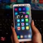 Hands holding smartphone displaying social media apps folder with Instagram, TikTok, WhatsApp, Facebook, Twitter, YouTube and other popular apps that use Android app cache for faster loading and performance.