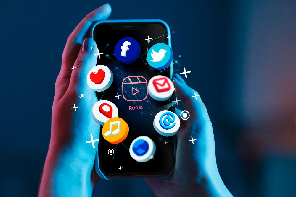 Hands holding a smartphone with floating app icons including Facebook, Twitter, heart, location pin, music, video, email, and browser apps against a blue gradient background with sparkle effects