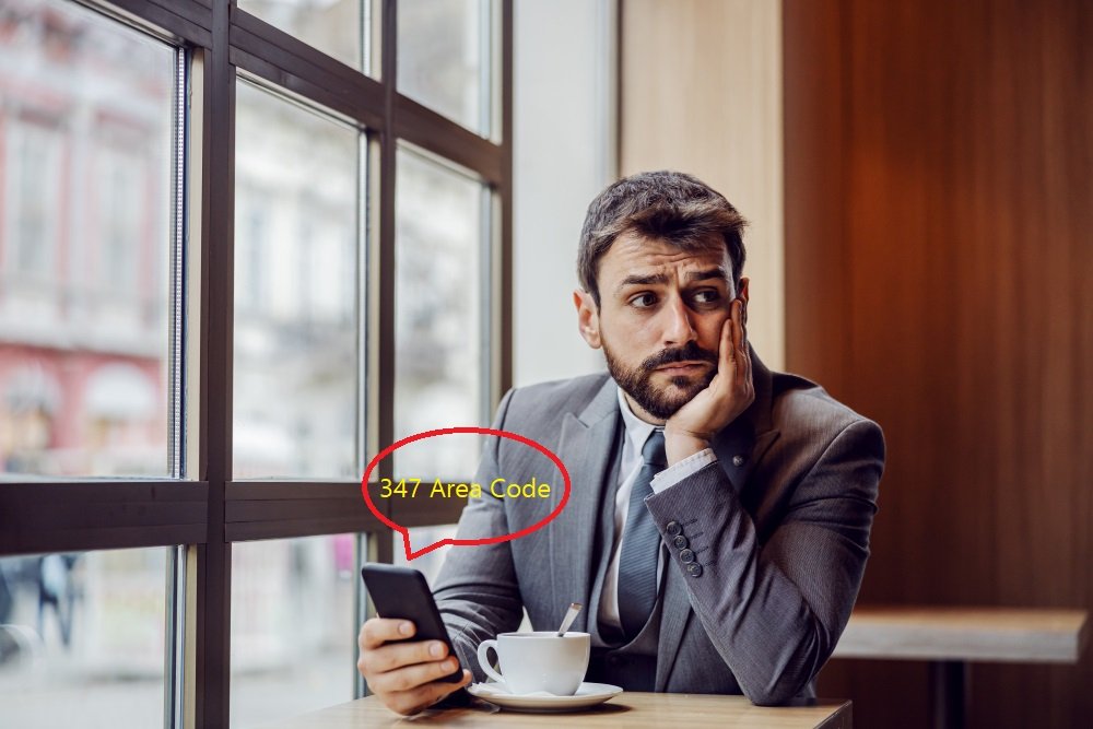 Concerned businessman in suit looking at smartphone displaying 347 Area Code call while sitting by window with coffee