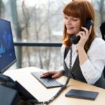 Woman in business attire talking on landline phone at desk, demonstrating North American Numbering Plan telecommunications in office